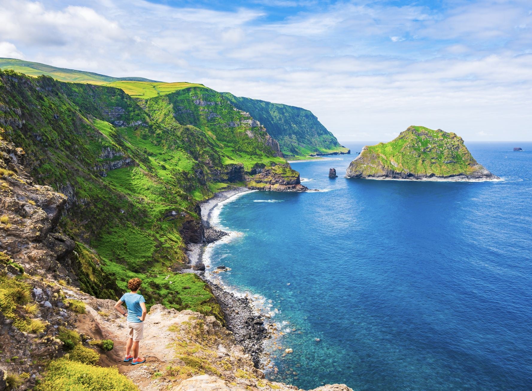 Jeune femme touristique regardant la magnifique baie avec plage et falaises vertes à Baia de Alem, île de Flores, Açores, Portugal