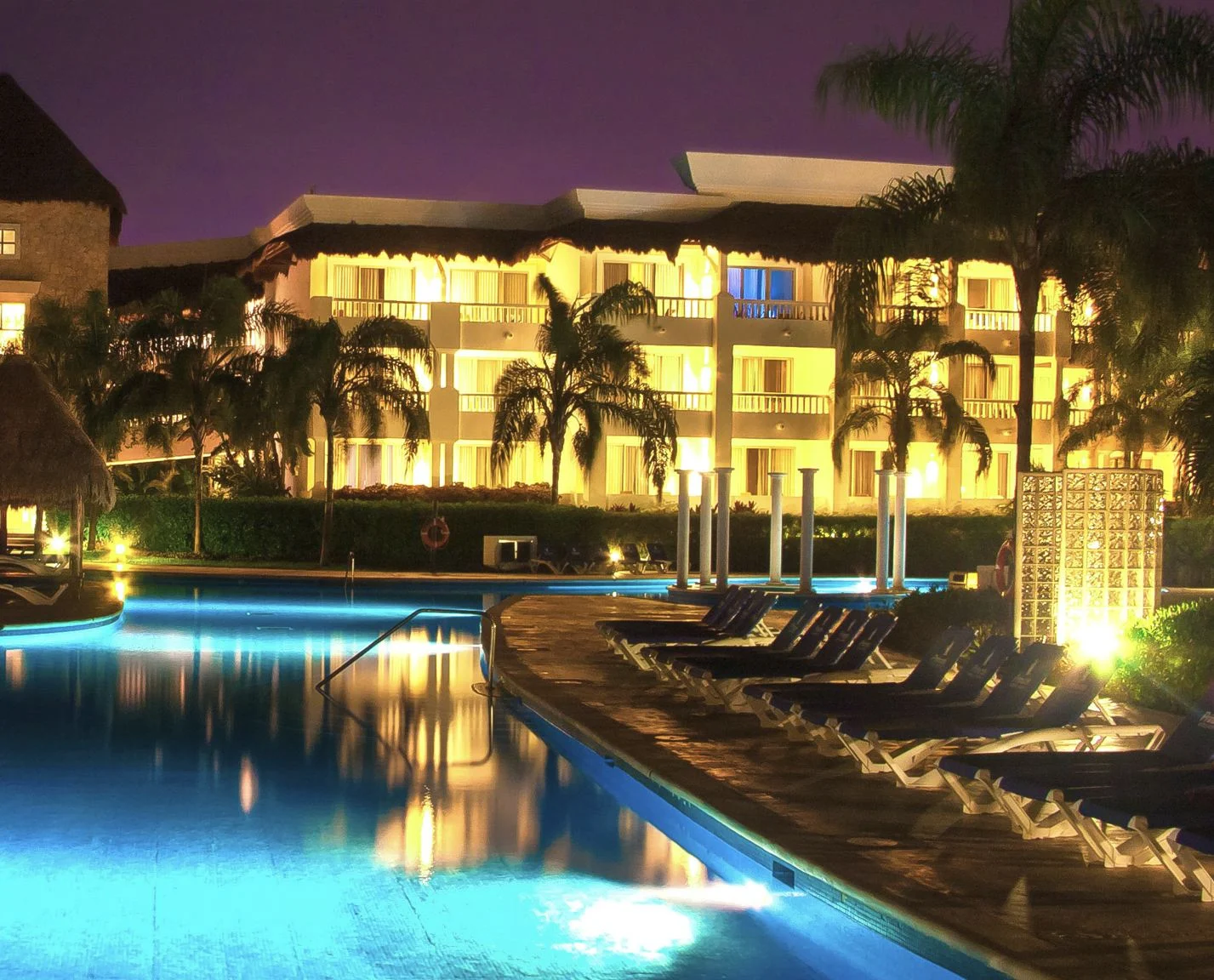 Resort la nuit avec stores ouverts sur la chambre depuis la piscine