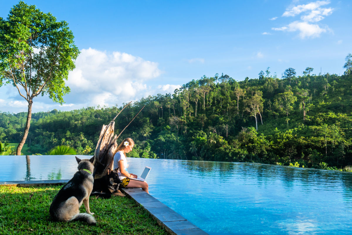 Belle jeune femme avec une fleur sur la tête travaille en ligne sur un ordinateur portable à côté de la piscine et d'un arrière-plan pittoresque près de Galle, Sri Lanka