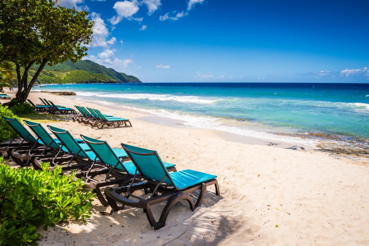 Sainte-Croix, Îles Vierges américaines Deux rangées de chaises longues en tissu bleu sarcelle bordent une plage de sable blanc avec une vue sur la magnifique mer des Caraïbes.