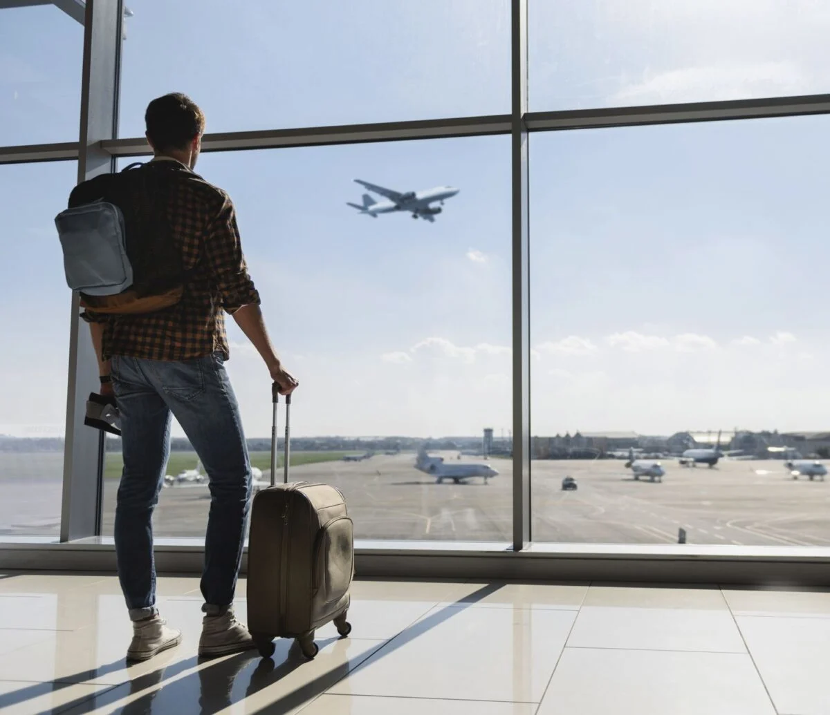 Un jeune-homme-est-debout-près-de-la-fenêtre-à-l'aéroport-et-regarde-l'avion-avant-le-départ.