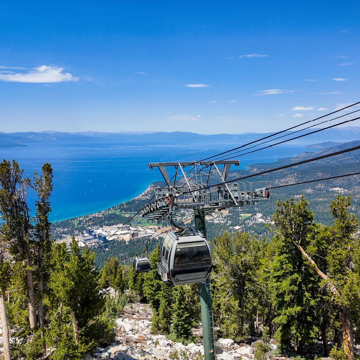 Une balade sur la télécabine du lac Tahoe en regardant le système de câbles et les voitures avec le lac Tahoe et la montagne en arrière-plan pendant que les gens montent et descendent la montagne.